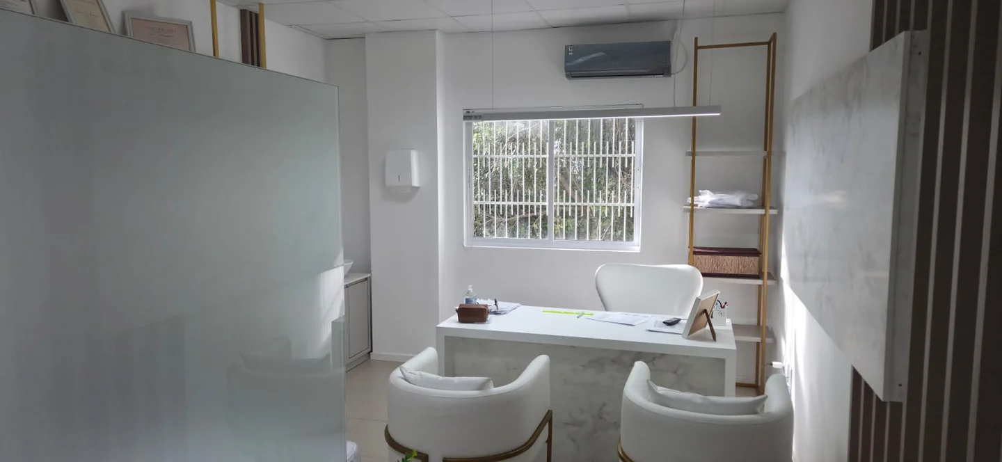 Consultório da clínica com poltronas brancas, mesa de atendimento e luz natural